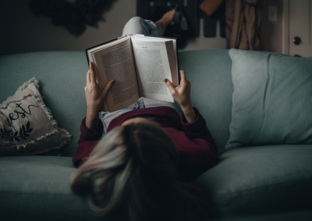 Girl reading book with legs over sofa